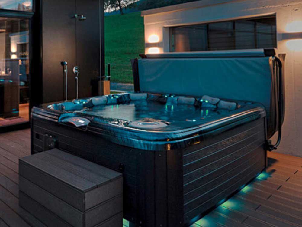 Hot tub with illuminated features and a cover, surrounded by a stylish deck, showcasing a relaxing spa environment for maintenance and service options.