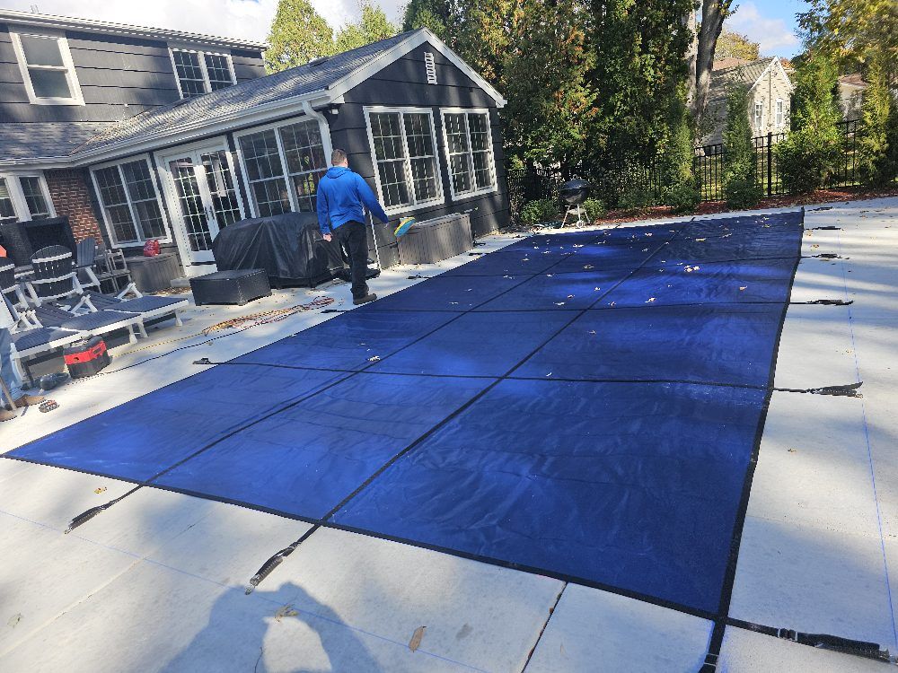 Person installing a blue safety pool cover on a residential patio, showcasing durability and protection for the pool area.