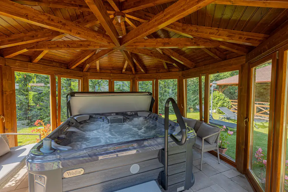 Wellis spa in a wooden gazebo, surrounded by greenery and outdoor furniture, showcasing a relaxing spa environment for maintenance and cleaning services.