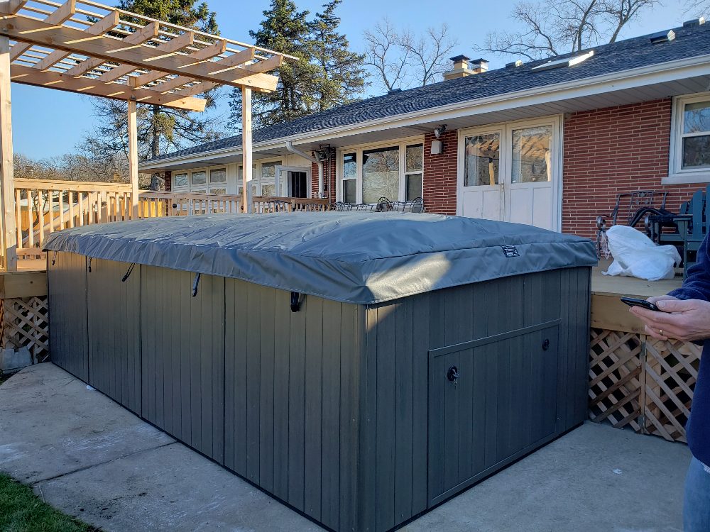 Spa with cover in residential backyard, surrounded by wooden deck and house, illustrating winter spa preparation services.