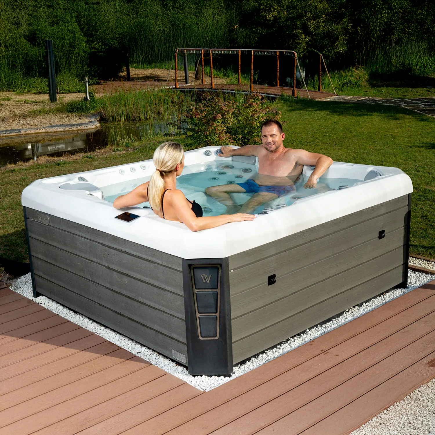 Couple enjoying a Wellis hot tub in a serene outdoor setting, featuring hydro massage jets and a modern design, ideal for relaxation and comfort.