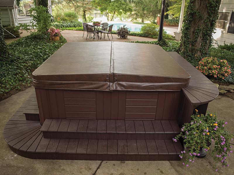 Manual spa cover on a hot tub in a landscaped backyard, showcasing energy efficiency and protection for hydrotherapy use.