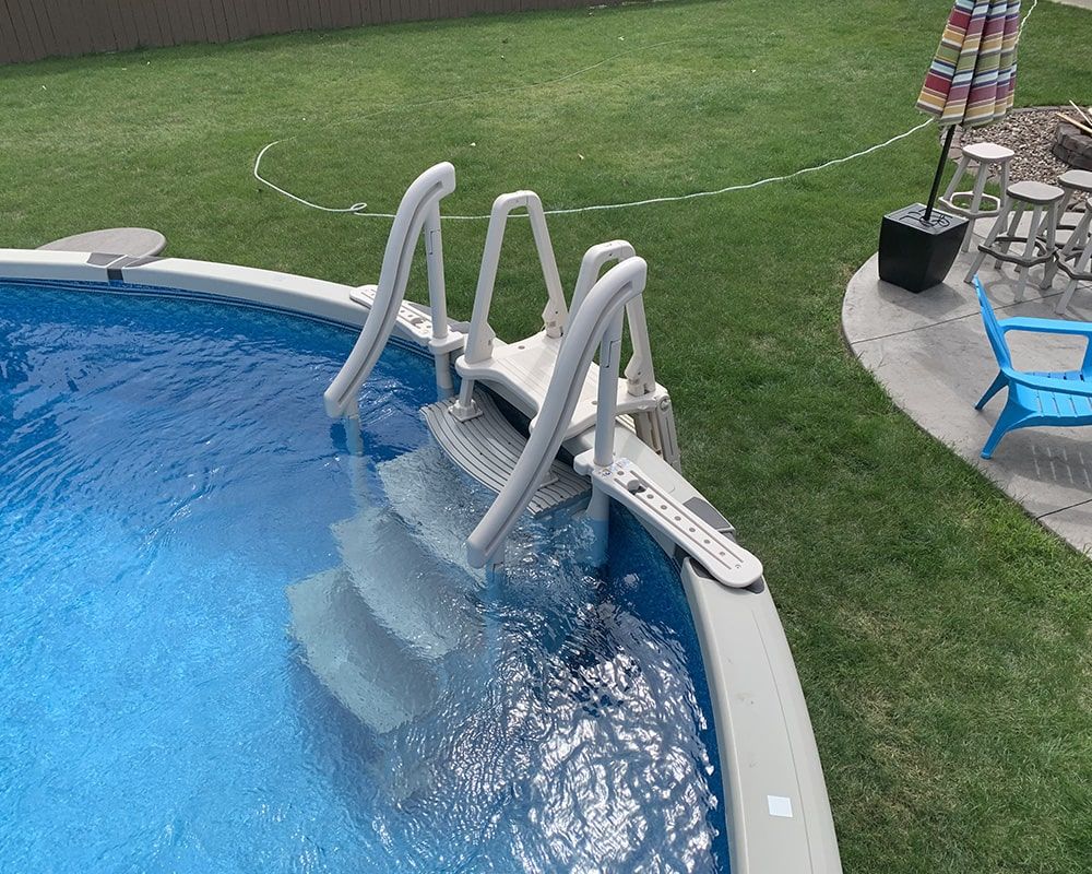 Pool ladder and entry steps in a residential above-ground pool, surrounded by green grass and outdoor furniture, emphasizing quality outdoor leisure equipment.