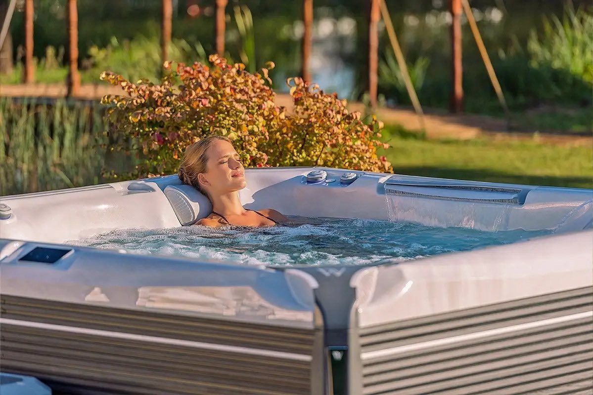 Woman relaxing in a hot tub surrounded by greenery, showcasing spa features relevant to Leisure Pools and Spas maintenance services.