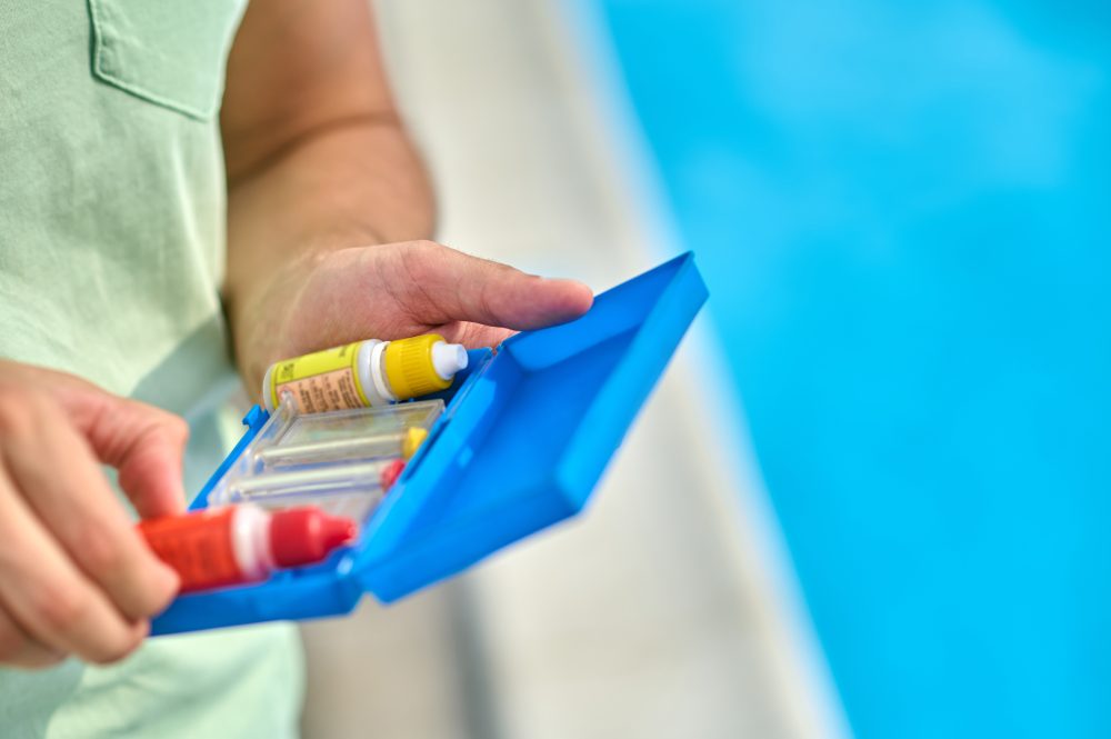 Pool water testing kit with colorful reagents held by a technician, emphasizing water analysis services for pool maintenance and troubleshooting.
