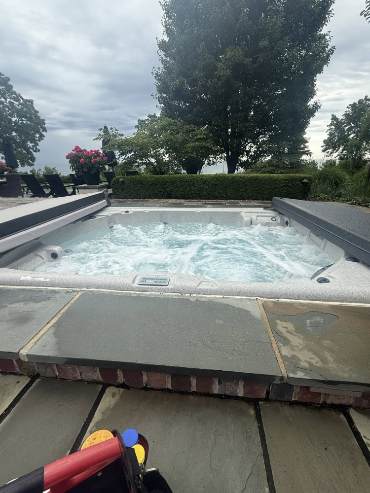 Hot tub with bubbling water and control panel, surrounded by lush greenery and flowers, illustrating spa maintenance services.