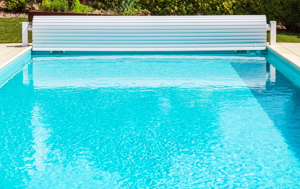 Solar pool cover roller shutter partially covering a swimming pool, showcasing energy-efficient and protective features for pool maintenance.