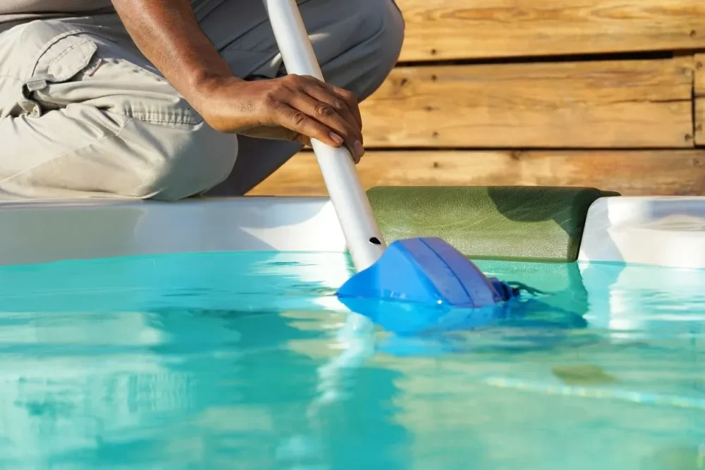 Person using a pool vacuum to clean a swimming pool, emphasizing routine maintenance and water clarity.