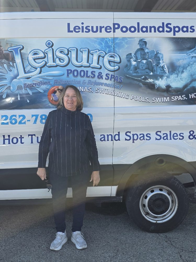 Woman standing in front of a Leisure Pools & Spas service vehicle, showcasing the company logo and services related to pools and hot tubs.
