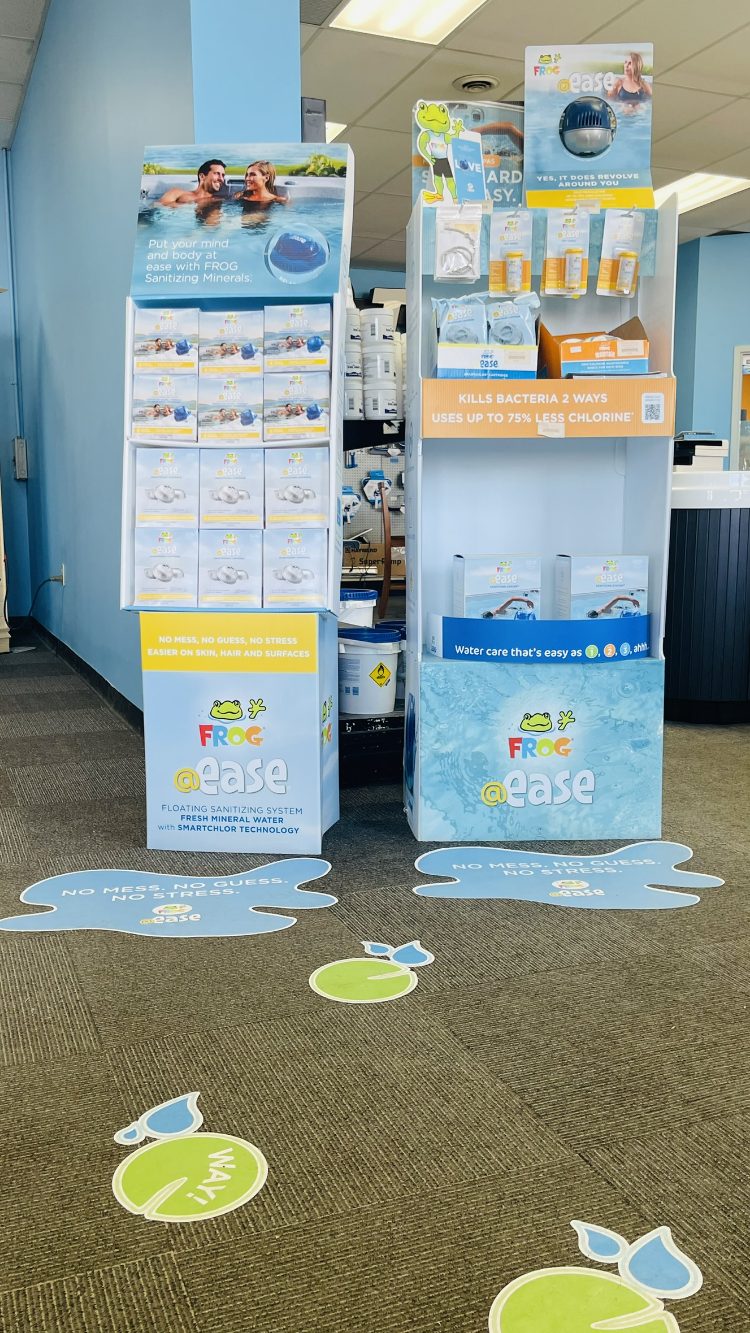 Display of FROG @ease pool sanitizing products, featuring promotional signage and colorful floor decals, in a Leisure Pools & Spas store, emphasizing ease of use and reduced chlorine requirements.
