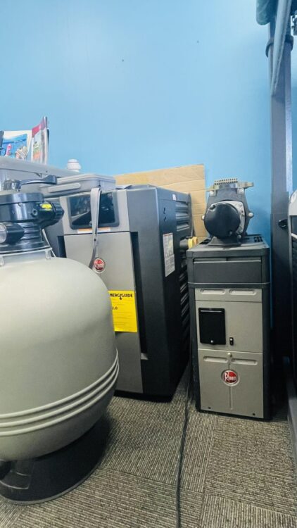 Pool and spa equipment display featuring a large gray sand filter, a heater, and a pump in a store setting, emphasizing quality outdoor leisure products.
