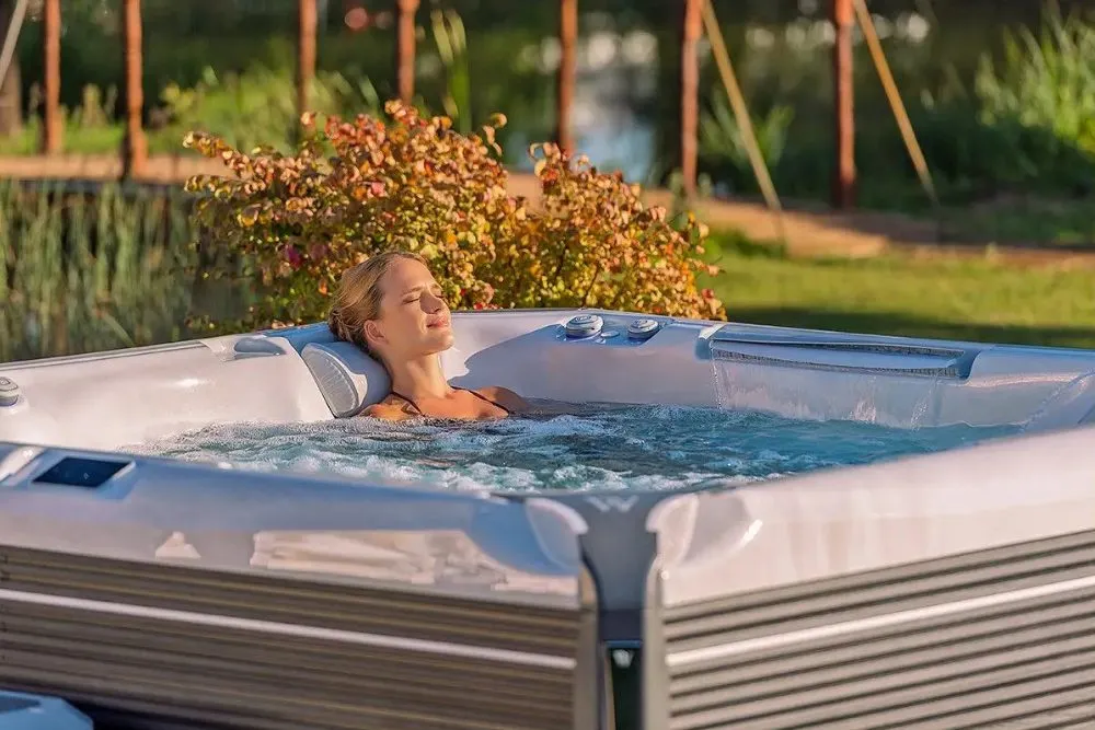 Woman relaxing in a hot tub surrounded by greenery and a serene setting.